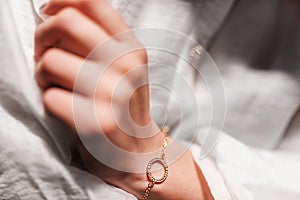 Gold bracelet in the form of a ring with diamonds on a chain, girlâ€™s hand, sleeve of a white shirt, dark background