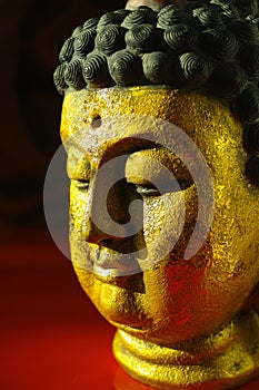 Gold Buddha tranquil face on dark red background, copy space