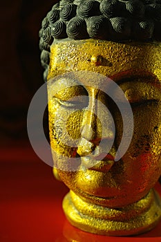 Gold Buddha tranquil face on dark red background, copy space