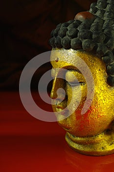 Gold Buddha tranquil face on dark red background, copy space