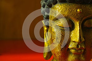 Gold Buddha tranquil face on dark red background, copy space