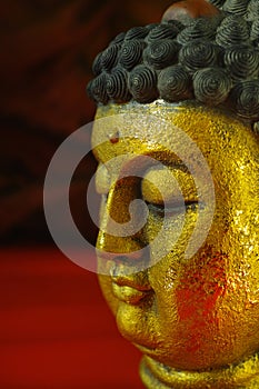 Gold Buddha tranquil face on dark red background, copy space