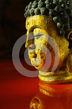 Gold Buddha tranquil face on dark red background, copy space