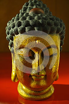 Gold Buddha tranquil face on dark red background, copy space