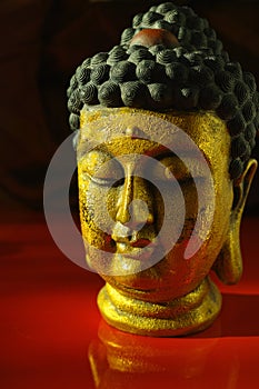 Gold Buddha tranquil face on dark red background, copy space