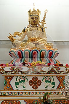 A gold Buddhist Guru Rinpoche Padmasambhava statue sitting on a colourful pedestal