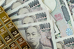 gold bullion ingot and pile of japanese yen banknotes as financial safe haven or investment concept