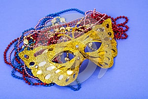 Gold carnival mask with colored beads on violet background