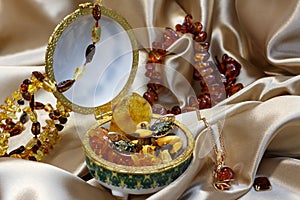 Gold chain with amber pendant. Baltic amber in Ceramic casket, amber necklace and bracelet on a pastel background satin.