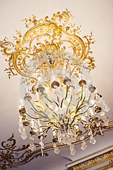 Gold chandelier crystal with gold decorative elements on the ceiling in the Baroque style
