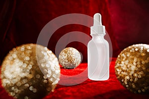 Gold christmas balls and face serum on red background