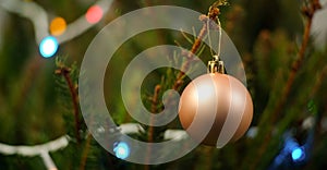 Gold Christmas bauble on branch of a real Christmas tree with bokeh lights in background