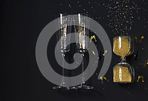 Gold christmas flat layout with confetti, two champagne glasses and hourglass on black background. New Year festive concept. Top