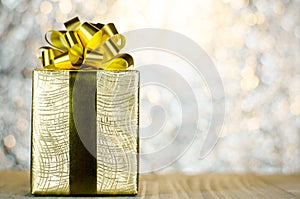 Gold Christmas gift box with ribbon and bow on bokeh lights back