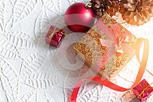 Gold christmas gift box tied in ribbon with red bauble on white paper texture