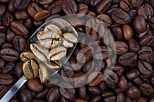 Gold coffee beans on a pile of coffee beans. The concept of luxury and originality. Golden coffee beans in a spoon. Coffee beans t