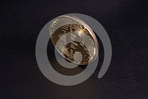 gold coin bitcoin stands upright on black leather