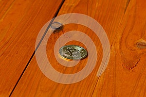 Gold coin of cryptocurrency Bitcoin in the rays of the rising sun on the background of an orange wooden textured table