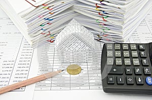 Gold coin in front of house with pencil and calculator