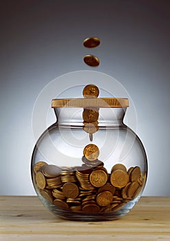 Gold coins dropping into glass jar