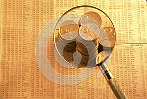 Gold coins on stock index under magnifying glass