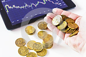 Gold coins and tablet placed on a white table showing a graph