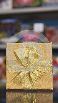 Gold-colored gift box with gold bow stands on the surface.