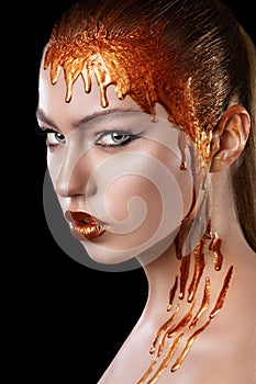 Gold colors flow down from the lips, face and neck of a beautiful model girl, creative abstract makeup.