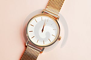 Gold coloured feminine wrist watch on a pink background. Just before 12 o clock. New year concept.