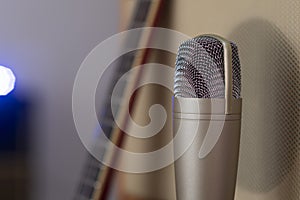 Gold condenser microphone in front of an amplifier speaker with a guitar and a blue led light on the background