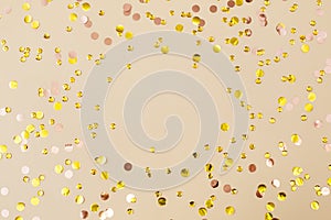 Gold confetti on beige paper background. Festive holiday backdrop. Birthday congratulations Christmas New Year.