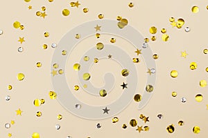 Gold confetti on beige paper background. Festive holiday backdrop. Birthday congratulations Christmas New Year. Flat lay  top view