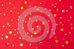 Gold confetti on red paper background. Festive holiday backdrop. Birthday congratulations Christmas New Year. Valentines Day.