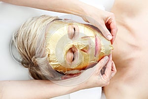 Gold cosmetic mask, the beautician applies a gold mask to a woman`s face. photo