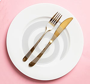 Gold cutlery and dishes set against pink background, formal place setting