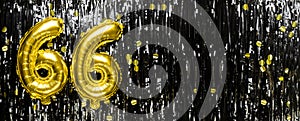 Gold foil balloon number number 66 on a background of black tinsel decoration. Birthday greeting card, inscription sixty
