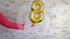 Gold foil balloon numeral 8 in femine hand. Happy Womens Day , copy space