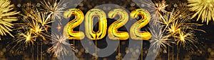 Gold foil balloons numeral 2022 and golden firework on dark black wooden texture - HAPPY NEW YEAR - Festive silvester New Year`s