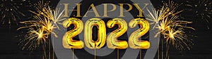 Gold foil balloons numeral 2022 and golden firework on dark black wooden texture - HAPPY NEW YEAR - Festive silvester New Year`s