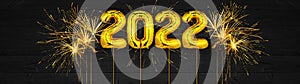 Gold foil balloons numeral 2022 and golden firework on dark black wooden texture - HAPPY NEW YEAR - Festive silvester New Year`s