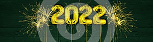 Gold foil balloons numeral 2022 and golden firework on dark green wooden texture - HAPPY NEW YEAR - Festive silvester New Year`s