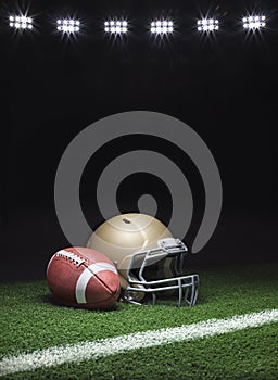 A gold football helmet and football on a grass field with stripe on dark background with stadium lights