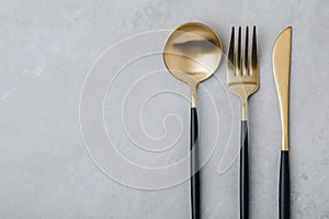 Gold fork, knife and spoon on gray stone background