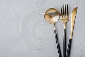 Gold fork, knife and spoon on gray stone background