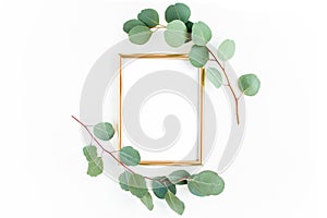 Gold frame is decorated with green branches and eucalyptus leaves on a white background. lay flat, top view