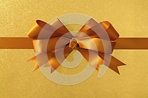 Gold gift bow ribbon, shiny metallic foil paper background, horizontal