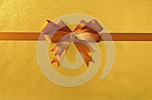 Gold gift bow ribbon, shiny metallic foil paper background, straight horizontal