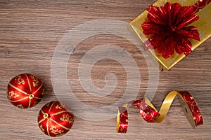 Gold gift box with red bouquet with red christmas bulbs and wrapping tape on a wooden table. Top view