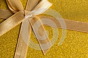 Gold gift box with ribbon and bow on shiny gold background. Top view.