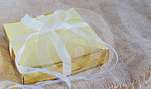 Gold gift box with white ribbon on the brown sack